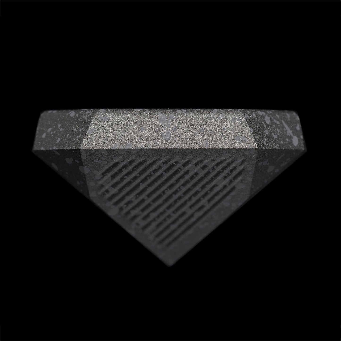 A detailed view of the Nyht Whisky Decanter lid right-side up. The close-up image highlights the detail of the precision machined aluminum list and the splatter paint finish. From this view, the lid takes on the form of an upside-down metal pyramid with facets on the corner that mimic the details in the base of the glasses.