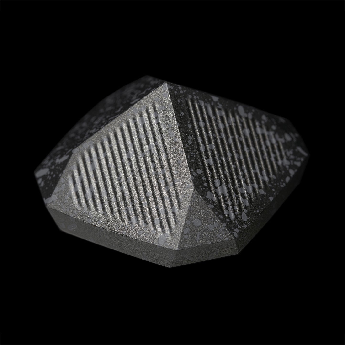 A detailed upside view of the Nyht Whisky Decanter lid with the bottom of the lid in view. The close-up image highlights the detail of the precision machined aluminum list and the splatter paint finish. From this view, the lid takes on the form of a metal pyramid with facets on the corner that mimic the details in the base of the glasses.