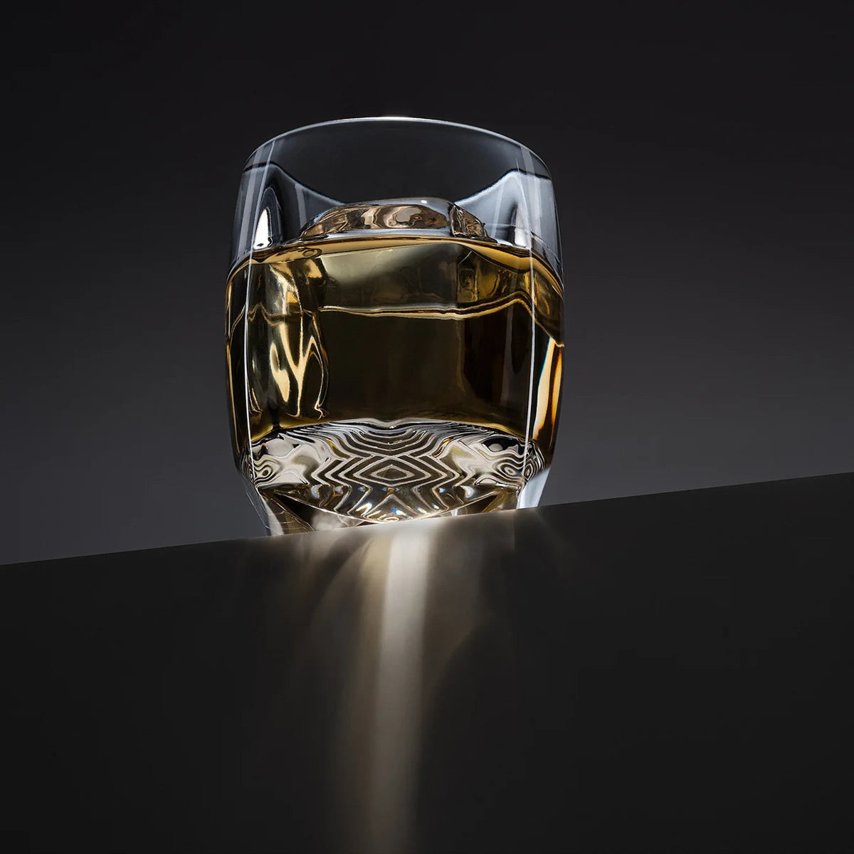 Rauk Heavy Tumbler with ice, resting on a dark gradient surface, illuminated by dramatic lighting that highlights its faceted crystal design and reflective clarity.